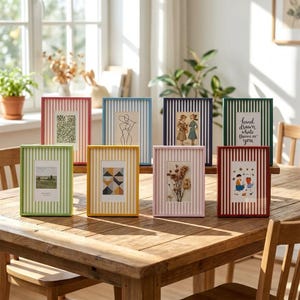 May include: A collection of eight rectangular picture frames in various colors, including red, light blue, dark blue, green, yellow, and pink, all featuring a vertical white stripe pattern and containing diverse art prints.