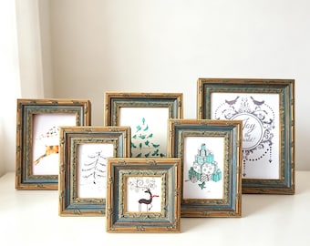 May include: A collection of six rectangular picture frames with ornate, distressed gold and blue-grey finishes. Each frame contains a unique holiday-themed illustration, including a reindeer, a Christmas tree, and text reading Joy to the World.
