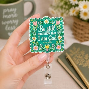 May include: A square badge reel with a scalloped edge featuring a teal background, floral illustrations in pink, yellow, and white, and the text "Be still and know that I am God" in white lettering, with "PSALM 46:10" printed in smaller white text below.