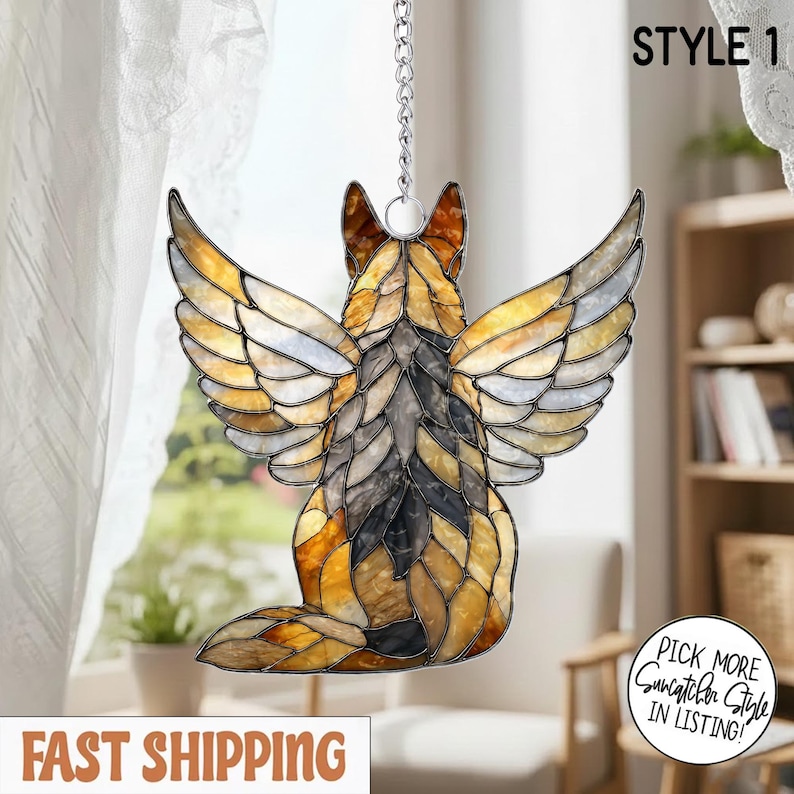 May include: A stained glass suncatcher shaped like a dog with wings, featuring amber, brown, and grey glass pieces held together by dark metal lines. The piece hangs from a silver-colored metal chain and includes the text STYLE 1 at the top.