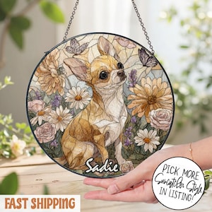 May include: Round stained glass suncatcher featuring a Chihuahua dog with the name "Sadie" and floral and butterfly accents. The suncatcher is suspended by a chain. The words "Pick More Suncatcher Style In Listing!" are in a circle.