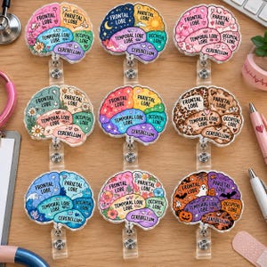 Op de afbeelding: Negen badgehouders in de vorm van een brein met gelabelde anatomische secties, waaronder de frontale, pariëtale, temporale en occipitale kwabben en het cerebellum. Elk brein toont unieke kleurrijke patronen, bloemmotieven, hemelse thema's of seizoensprints.