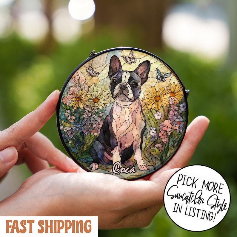 May include: Round stained glass suncatcher featuring a Boston Terrier dog surrounded by flowers and butterflies. The dog is black and white, with the name "Coca" written below. The suncatcher has a black metal frame.