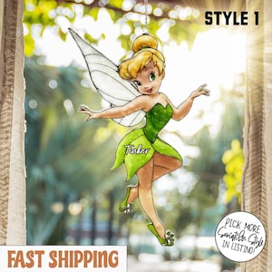 Puede incluir: Un atrapasoles con una hada de dibujos animados con cabello rubio, vestido verde y alas blancas. El hada está en una pose dinámica, con la palabra "Tinker" en su vestido. El atrapasoles está colgado de una cadena, con el texto "STYLE 1" en la parte superior.