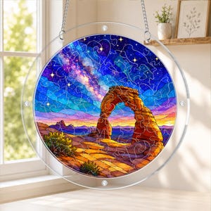 May include: A circular suncatcher featuring a vibrant puzzle-style illustration of a natural stone arch under a starry night sky. The design displays a colorful landscape with shades of orange, purple, and blue, suspended by silver chains.