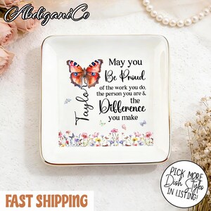 Può includere: Un piatto quadrato in ceramica bianca con bordo dorato, con un'illustrazione di farfalla e il testo "May you Be Proud of the work you do, the person you are & the Difference you make." Il piatto ha anche un bordo floreale.