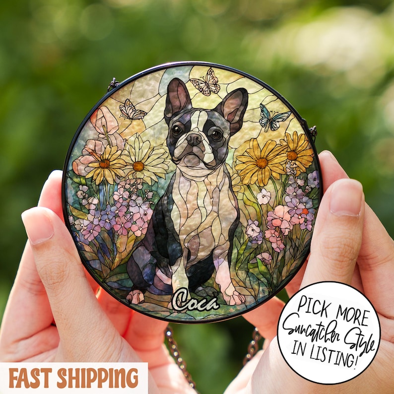 May include: Round stained glass suncatcher featuring a Boston Terrier dog in a garden setting with butterflies and flowers. The dog is black and white, with a name written below. The suncatcher has a black border and is held by a chain.