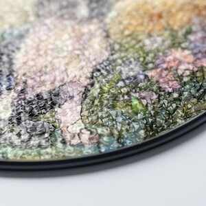 May include: A round decorative coaster with a colorful floral design. The coaster features a black edge and a textured surface with a variety of colors, including green, pink, and yellow. The coaster is designed to protect surfaces from drink rings.