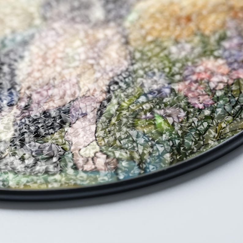 May include: A round decorative coaster with a colorful floral design. The coaster features a black edge and a textured surface with a variety of colors, including green, pink, and yellow. The coaster is designed to protect surfaces from drink rings.