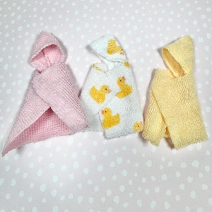 May include: Three hooded towels, one pink, one white with yellow rubber duckies, and one yellow. The towels are made of a soft, fluffy material.