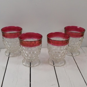 May include: Set of four clear glass drinking glasses with a red rim. The glasses have a textured, diamond-like pattern.
