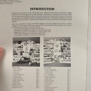 May include: A page from a cross-stitch pattern book. The page features an introduction, a list of designs, and a diagram of various cross-stitch patterns. The book includes designs for towels, baby bibs, and Christmas ornaments.