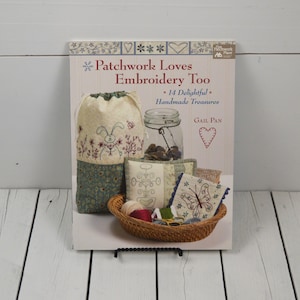 May include: Book cover featuring a patchwork design with the title "Patchwork Loves Embroidery Too" and the subtitle "14 Delightful Handmade Treasures" by Gail Pan. The cover shows a variety of embroidered items, including a bag, pillows, and a jar.