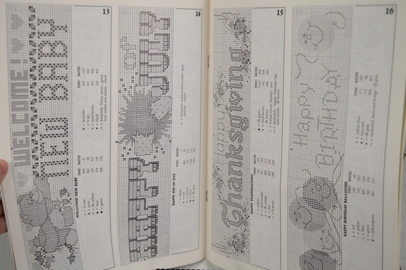 May include: A book page featuring cross-stitch patterns. Designs include "WELCOME NEW BABY", "HAPPY 4TH OF JULY", "HAPPY THANKSGIVING", and "HAPPY BIRTHDAY". Each design is accompanied by a color key and DMC floss numbers.