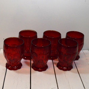 May include: Set of six red glass tumblers with a textured, raised design. The glasses have a rounded base and a wide mouth.