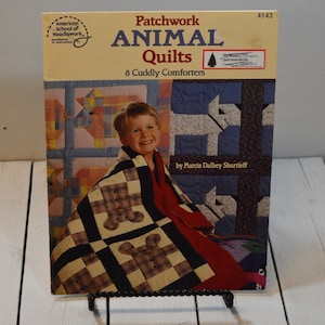 May include: A book cover with a patchwork animal quilt design. The title is "Patchwork Animal Quilts" with the subtitle "8 Cuddly Comforters". The book is by Marcia Dalbey Shurtleff.