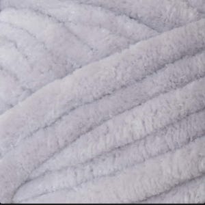 以下が含まれることがあります： 柔らかい、明るい灰色の糸のクローズアップ。糸は、太い編み物や編み物のプロジェクトを示唆する、目に見える隆起のある、豪華でビロードのような質感を持っています。色は、さまざまなクラフトプロジェクトに適した、落ち着いたニュートラルな色調です。