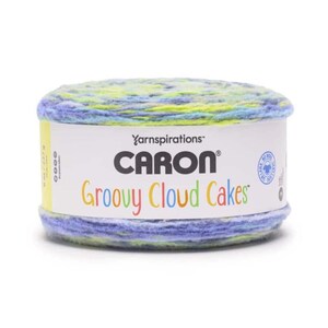 Puede incluir: Un ovillo de lana Caron Groovy Cloud Cakes. El hilo es una mezcla de azul, amarillo y verde. La etiqueta dice "Caron Groovy Cloud Cakes" en texto colorido. El hilo está en una bobina blanca.