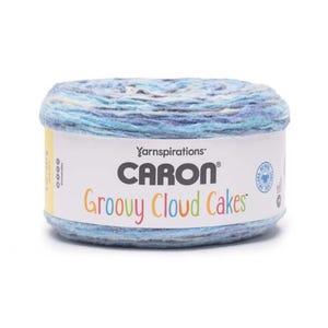 May include: A round skein of Caron Groovy Cloud Cakes yarn in shades of blue, white, and gray. The label features the Caron logo and the words "Groovy Cloud Cakes" in colorful letters. The yarn is ideal for knitting and crochet projects.