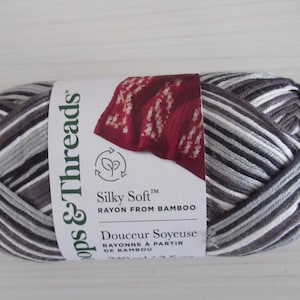 May include: A ball of yarn with a label that reads "Silky Soft Rayon From Bamboo". The yarn is a mix of gray, white, and black stripes. The label also features the words "Douceur Soyeuse" and a red fabric swatch.