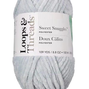 Pode incluir: Novel de fio de poliéster Sweet Snuggles da Loops & Threads, azul claro. O rótulo diz "Sweet Snuggles" e "Doux Câlins". O novelo contém 100 metros de fio e pesa 250 gramas.