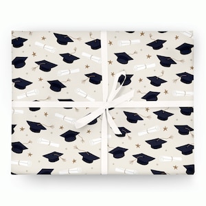 May include: Gift-wrapped package featuring a beige background with a repeating pattern of navy blue graduation caps, rolled diplomas, and gold stars. A white ribbon is tied around the package.