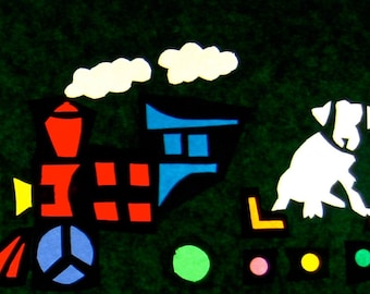May include: A green felt background with colorful paper cutouts of a sun, a mountain, a tree, two animals, a train, a dog, and flowers.