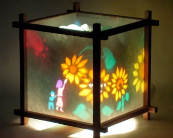 May include: A wooden lampshade with a light inside, featuring a colorful design of sunflowers and people. The lampshade is made of translucent paper and has a square shape.