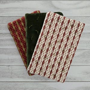 May include: Three quilted fabric pieces in red, green, and cream. The red piece has a repeating pattern of red and gold diamonds. The green piece is a solid velvet. The cream piece has a repeating pattern of red and gold ovals.