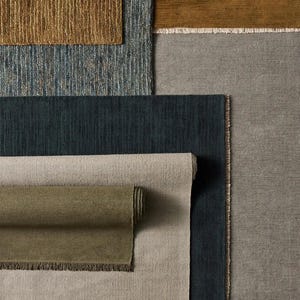 May include: A collection of rectangular rugs and fabric swatches in various textures and colors, including mustard yellow, slate blue, dark navy, olive green, beige, and gray, featuring fringed edges and woven patterns.