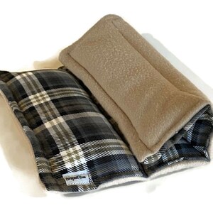Puede incluir: Un art&iacute;culo de tela rectangular y plegable que presenta un patr&oacute;n de cuadros en negro, blanco y gris en un lado y una textura s&oacute;lida de color beige tipo forro polar en el otro. Tiene una peque&ntilde;a etiqueta blanca con el texto "Ferapeutic".