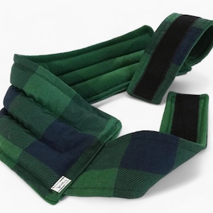 May include: A green and black plaid fabric neck wrap with a black velcro strap. The wrap is padded and has a label that says "The Warmth Co."