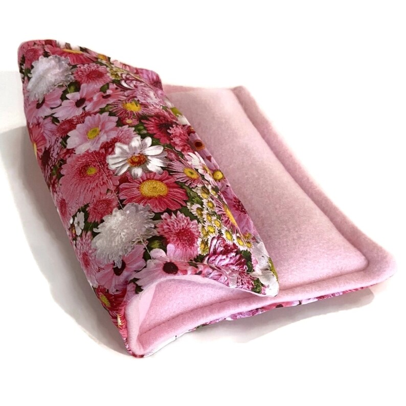 May include: A pink and floral patterned fabric bed for small pets, with a pink fleece lining. The bed is folded in half, showing the inside lining.