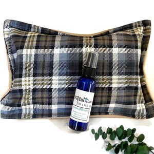 Plaid heating pad pillow with a blue spray bottle with a white label that reads 'Theraputic Calm give a warm hug Aromatherapy Essential Oil Spritzer for comfort packs'.