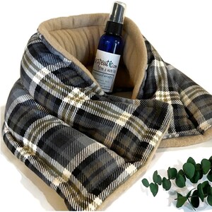 A gray, black, and white plaid neck wrap with a tan fleece lining. A small blue bottle with a white label that reads 'Therapetuc Calm give a warm hug Aromatherapy Essential Oil Diffuser Heat Packs' is inside the neck wrap.