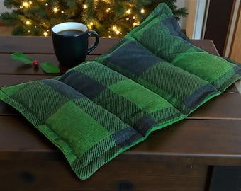 Puede incluir: Una almohadilla térmica rectangular con un patrón de cuadros escoceses en verde y negro. La tela está dividida en tres secciones horizontales distintas con costuras visibles, creando una apariencia acolchada en la superficie del artículo textil.