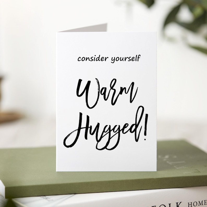 May include: White card with black calligraphy that reads "consider yourself warm hugged!"