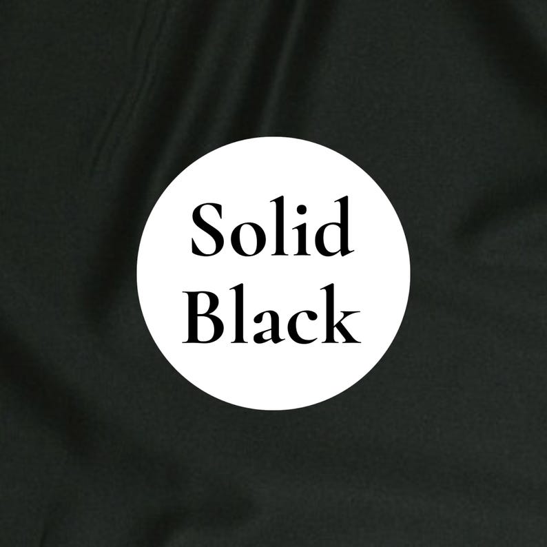 May include: A solid black fabric background featuring a centered white circle containing the black text Solid Black. The fabric has a smooth, matte texture with subtle folds and shadows that create a soft, uniform appearance across the surface.