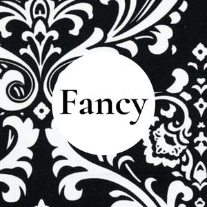 May include: A black and white damask patterned fabric featuring a central white circle with the word Fancy printed in black serif font. The intricate floral and scrollwork design covers the background in a high-contrast monochromatic color scheme.
