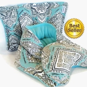 May include: A turquoise blue eye mask with a white and gray geometric pattern. The eye mask is made of soft fabric and is filled with flax seeds. The eye mask is a popular item for relaxation and sleep.