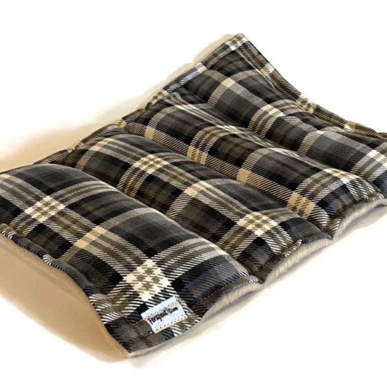 Puede incluir: Una almohadilla t&eacute;rmica rectangular de varias secciones con un patr&oacute;n de cuadros en gris oscuro, negro y blanco en la superficie superior. Una peque&ntilde;a etiqueta de tela blanca con el texto Fernsprout Lane est&aacute; cosida en la esquina inferior.