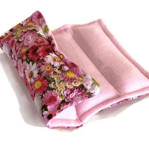 May include: A pink floral print fabric hot pack with a pink fleece outer layer. The hot pack is folded in half and has a seam down the center.