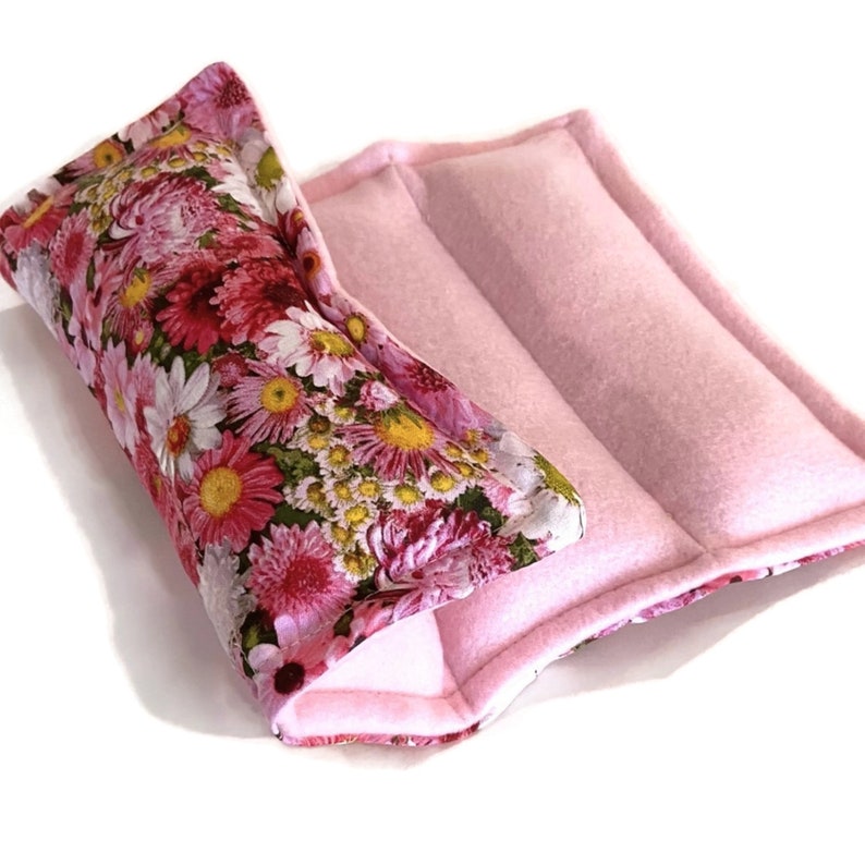 May include: A pink floral print fabric hot pack with a pink fleece outer layer. The hot pack is folded in half and has a seam down the center.