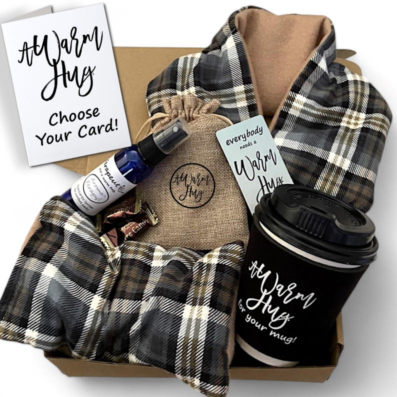 May include: A gift box filled with self-care items, including a plaid scarf, a small burlap bag with a brown label that says "#Warm Hug", a bottle of aromatherapy spray, a card that says "everybody needs a warm hug", a mug with a black sleeve that says "#Warm Hug for your mug!" and a few chocolate candies.