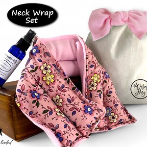 K&ouml;nnte beinhalten: Ein Nackenw&auml;rmer-Set bestehend aus einem rosa Stoffwickel mit gelbem und blauem Blumenmuster, einer blauen Spr&uuml;hflasche mit dem Etikett Therapeutic und einem beigen Beutel mit rosa Schleife und dem Logo A Warm Hug.