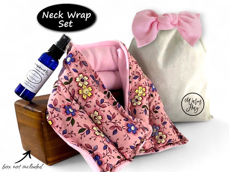 K&ouml;nnte beinhalten: Ein Nackenw&auml;rmer-Set bestehend aus einem rosa Stoffwickel mit gelbem und blauem Blumenmuster, einer blauen Spr&uuml;hflasche mit dem Etikett Therapeutic und einem beigen Beutel mit rosa Schleife und dem Logo A Warm Hug.