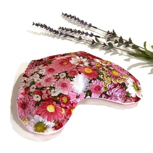 May include: A pink floral print eye pillow with a curved shape. The pillow is filled with flax seeds and lavender.