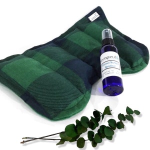 May include: A green and black plaid fabric heating pad with a blue bottle of aromatherapy spritzer. The bottle has a white label with the text "Aromatherapy Spritzer" and "Essential Oil Comfort Pack".