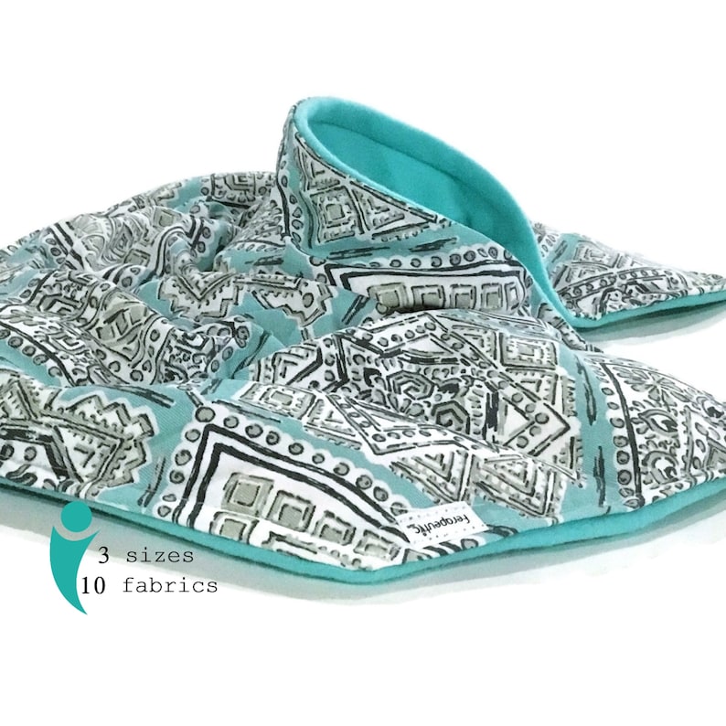 A turquoise and white patterned fabric neck  and shoulder heat wrap with a turquoise fleece lining. The fabric has a geometric pattern with black and gray accents. Hot Cold Pack for microwave designed for relaxation and pain. The text below the fabric reads '3 sizes 10 fabrics.'