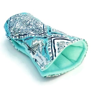 May include: A turquoise blue and white patterned fabric wrist wrap with a soft, light blue fleece lining. The wrist wrap is labeled "Therapeutic".